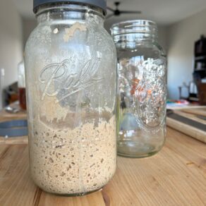 Ball jar with sourdough starter on butcher block island with jar and cutting board in background.